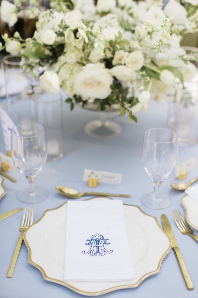 Blue wedding table with gold rimmed chargers, gold cutlery and custom monogram napkins