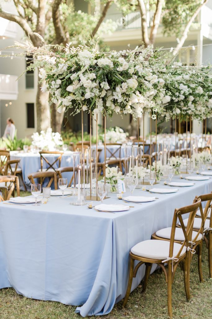Blue wedding tables with wood chairs and tall white flower centrepieces 