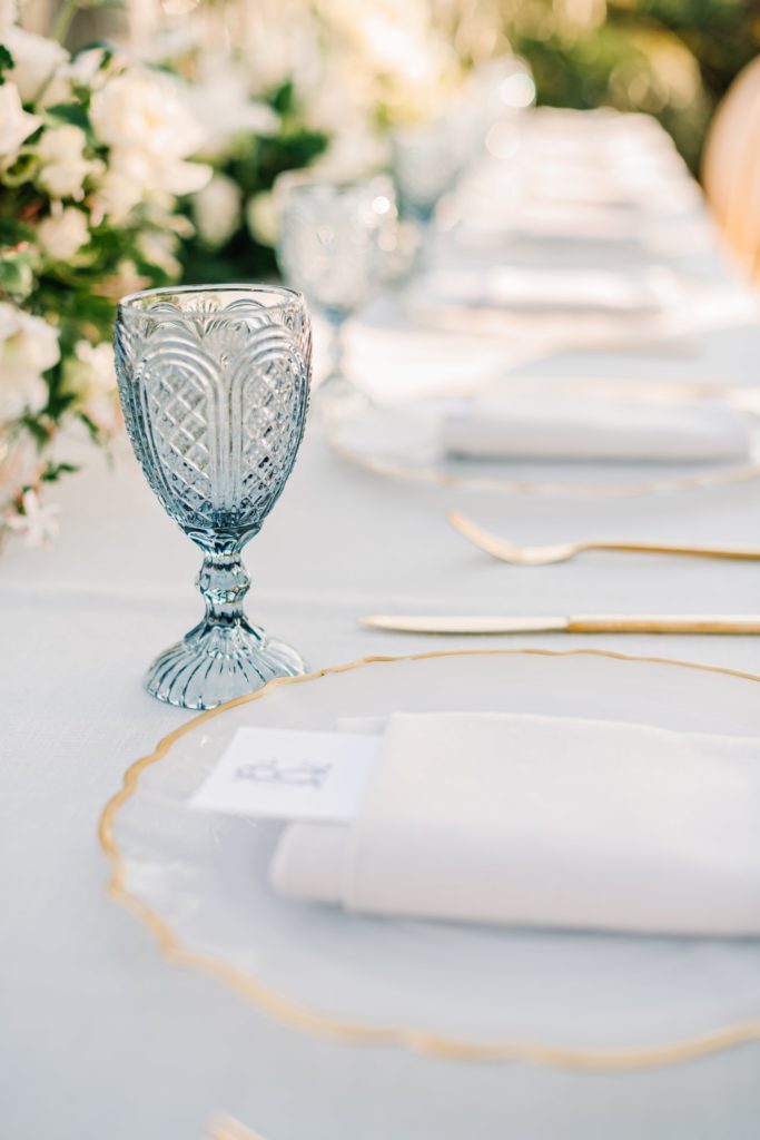 Wedding place setting with gold rimmed chargers and blue water goblets