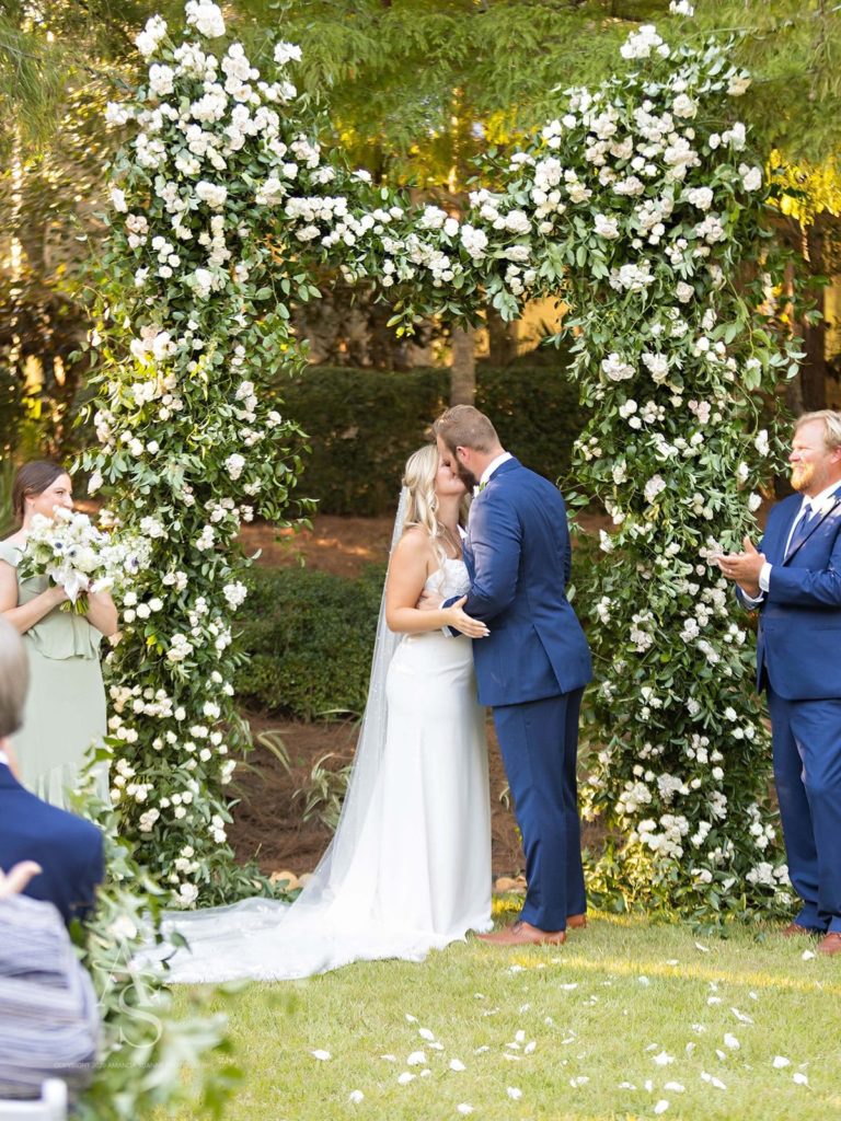 Bride and groom kissing under a floral wedding arch