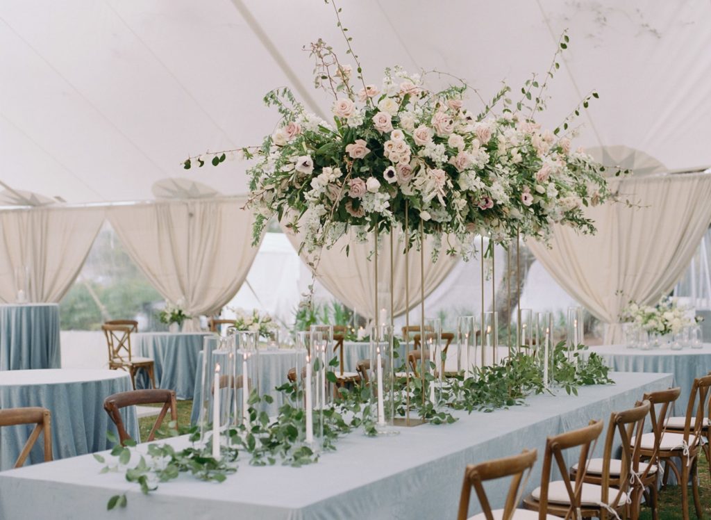 Long wedding table with light blue linens and tall floral arrangement 
