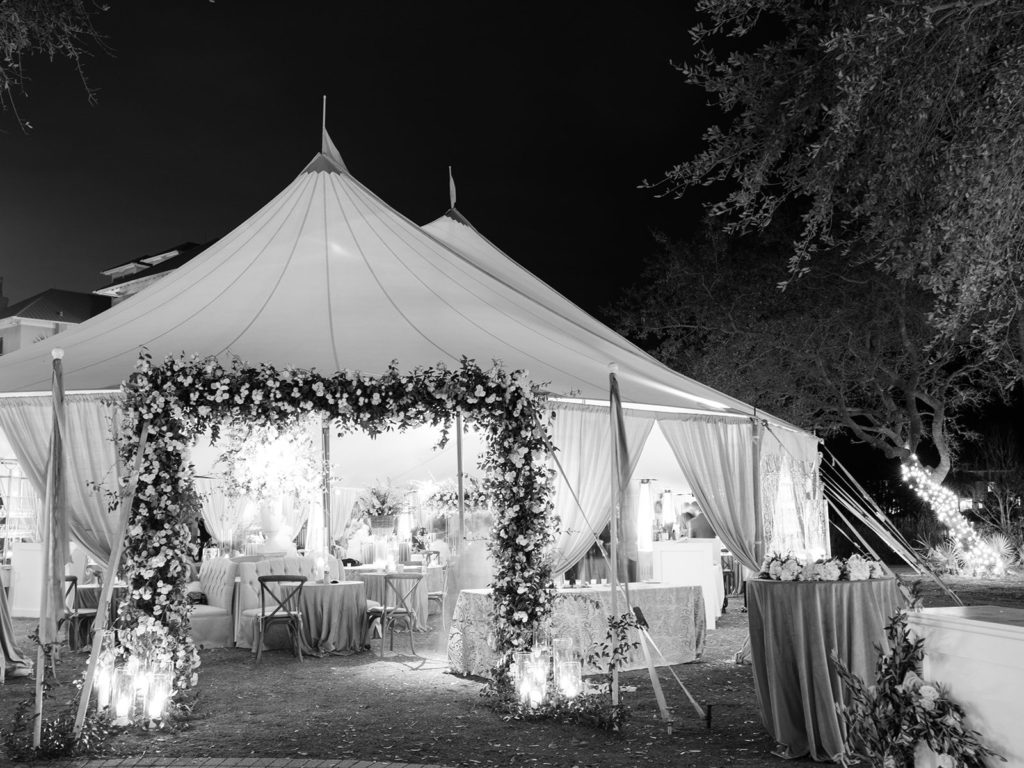 Black and white image of white sail tent with flower entrance 