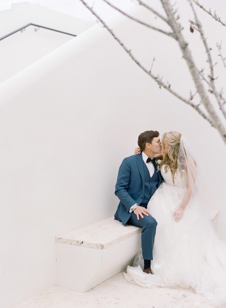 Bride and groom kissing in front of white wall