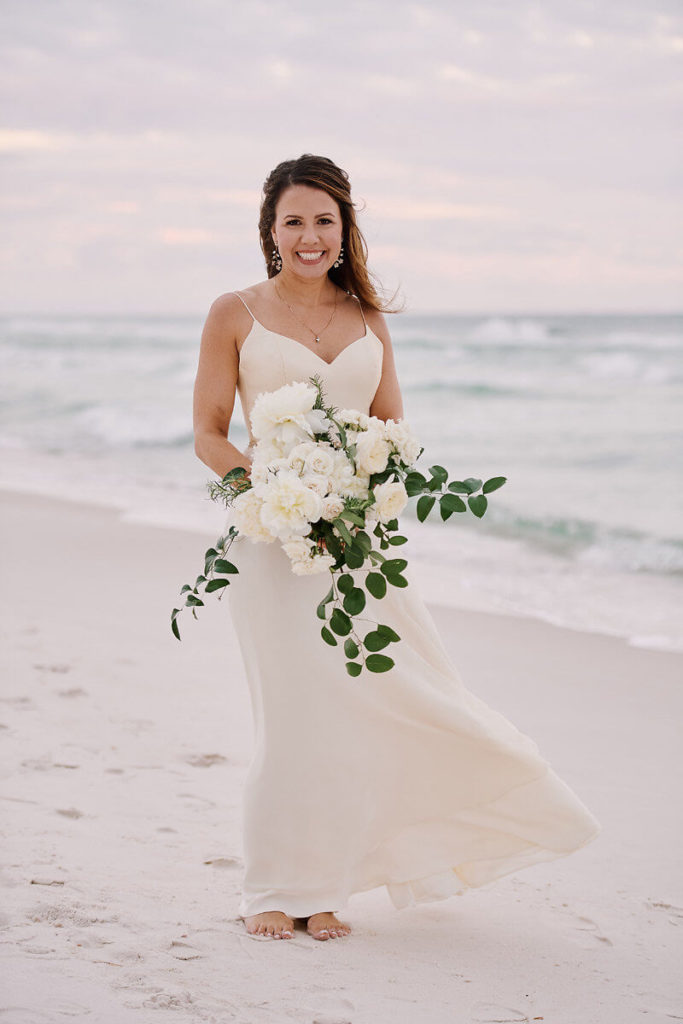Bride on beach holding white boquet at destination wedding
